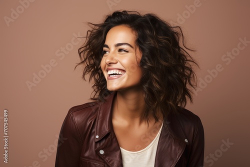 Happy smiling young woman in brown leather jacket looking at camera over brown background © Inigo