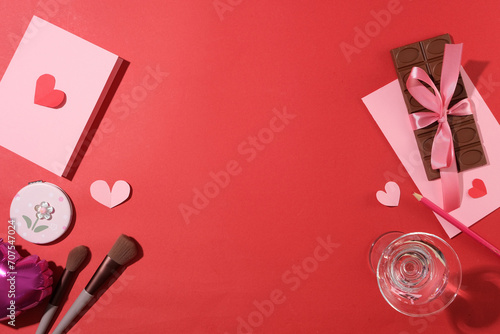 Chocolate bar, pink card, a cocktail glass, paper hearts and a makeup kit on a pink background. Ideal space for decoration on anniversaries. Copy space.