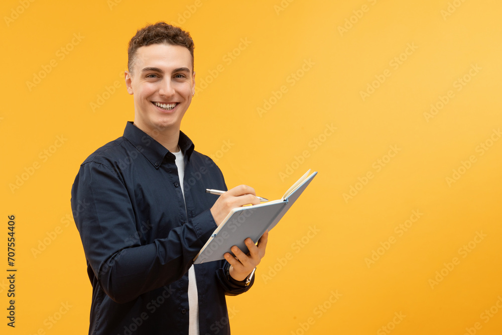 Cheerful young guy taking notes in notepad and smiling