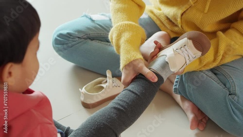 Asian mother helping her little son put on his shoes at home. First day of school.