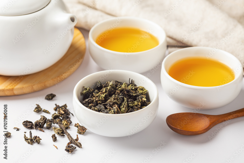 Tea leave in cup, closeup with tea set on white table Tea leave in cup, closeup with tea set on white table