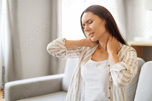 Young woman at home touching her neck with pained expression 
