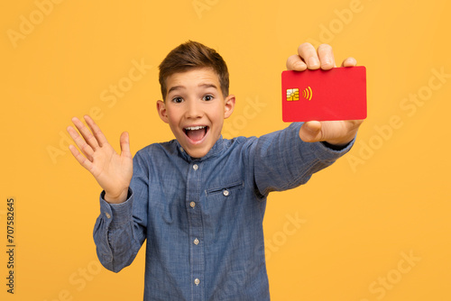 Happy surprised teen boy showing red credit card at camera photo