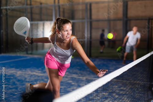 Young sporty woman padel player hitting ball with a racket on a hard court © JackF