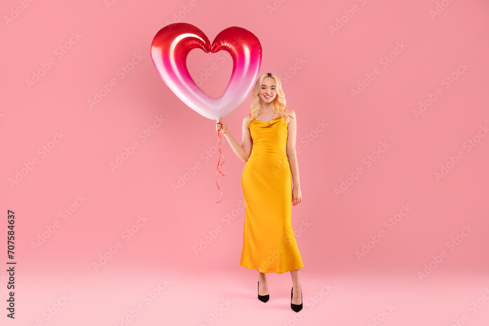 Elegant woman with a pink and white heart balloon on pink backdrop