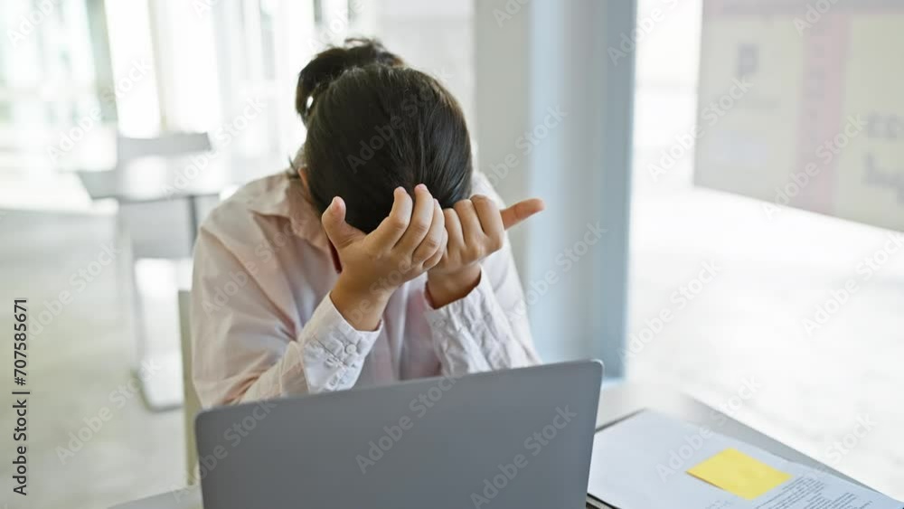 Stressed hispanic woman with glasses in office feeling overwhelmed by work, head in hands at her laptop. Stressed hispanic woman with glasses in office feeling overwhelmed by work, head in hands at her laptop.