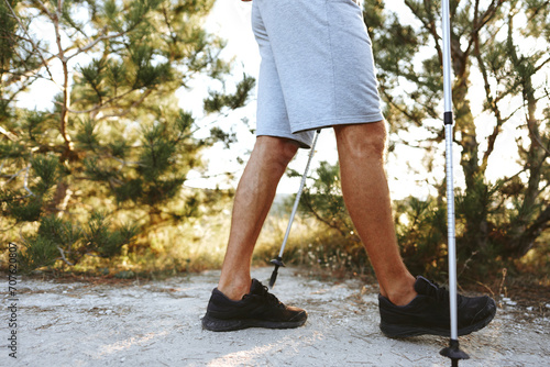 Male legs in comfortable hiking shoes with nordic walking poles on forest path