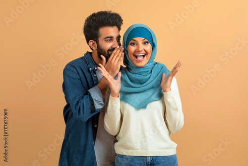 Delighted arab muslim couple sharing joyful secret, man whispering into woman's ear photo
