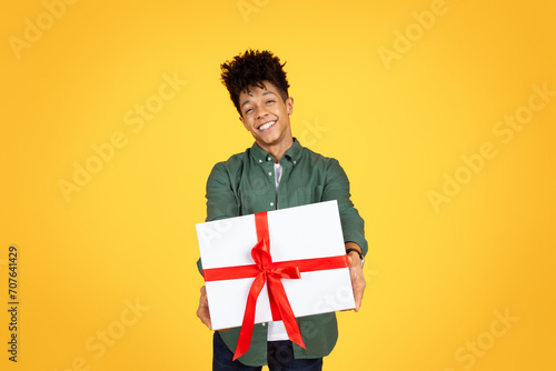 Happy handsome young black guy giving present, yellow background photo