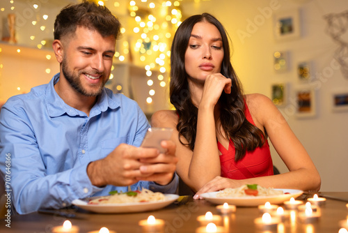Smiling man on phone  woman disenchanted at dinner