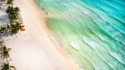 Aerial view of a tropical beach with clear turquoise waters, white sands, palm trees, and colorful kayaks, evoking a serene summer vacation setting