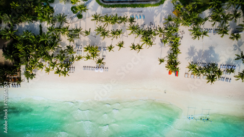 Aerial view of a tropical beach resort with palm trees, sun loungers, and turquoise sea, depicting a luxury summer vacation concept