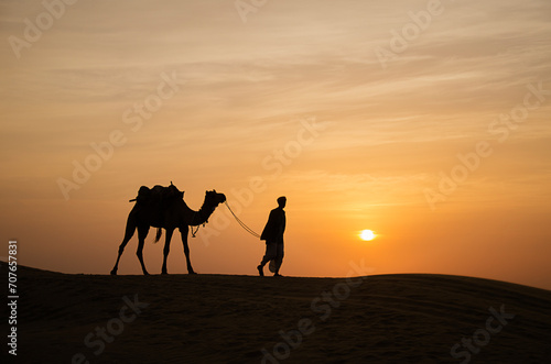 Camel man and camel during sunset with colorful sky at Jaisalmer sand dunes, Rajasthan, India, Asia. Background. Backdrop. Wallpaper.