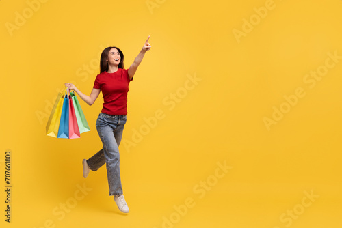 Excited young asian woman with shopping bags pointing copy space