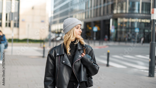 Urban stylish young fashion woman model in fashionable clothes with a knitted hat and leather jacket walking on the street