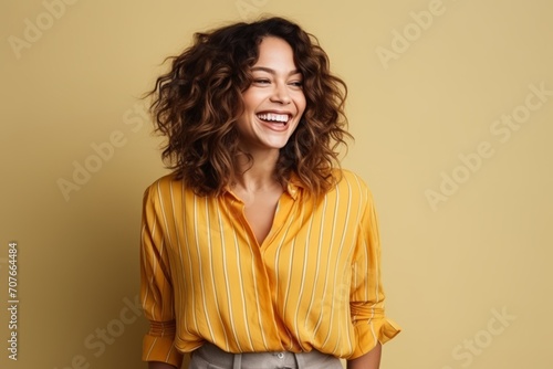 Portrait of a beautiful young woman laughing and looking at camera over yellow background