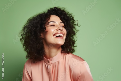 Portrait of a beautiful young woman with curly hair laughing on green background