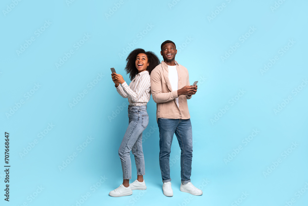 Fototapeta premium Excited african american couple with phones on blue background