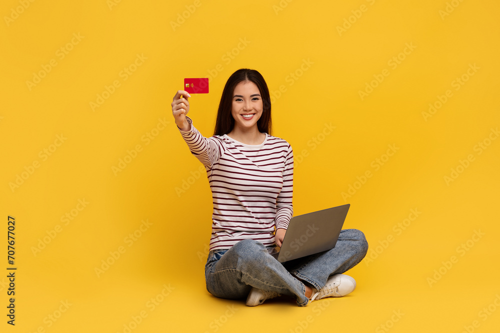 Cheerful young asian woman holding laptop and credit card - obrazy, fototapety, plakaty 