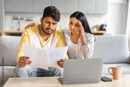 Bad News. Upset Indian Couple Reading Papers, Sitting On Couch At Home