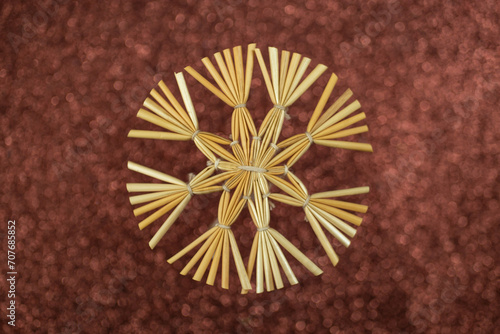 Christmas snowflake decoration made with golden straws and thread on brown glitter background, soft focus close up