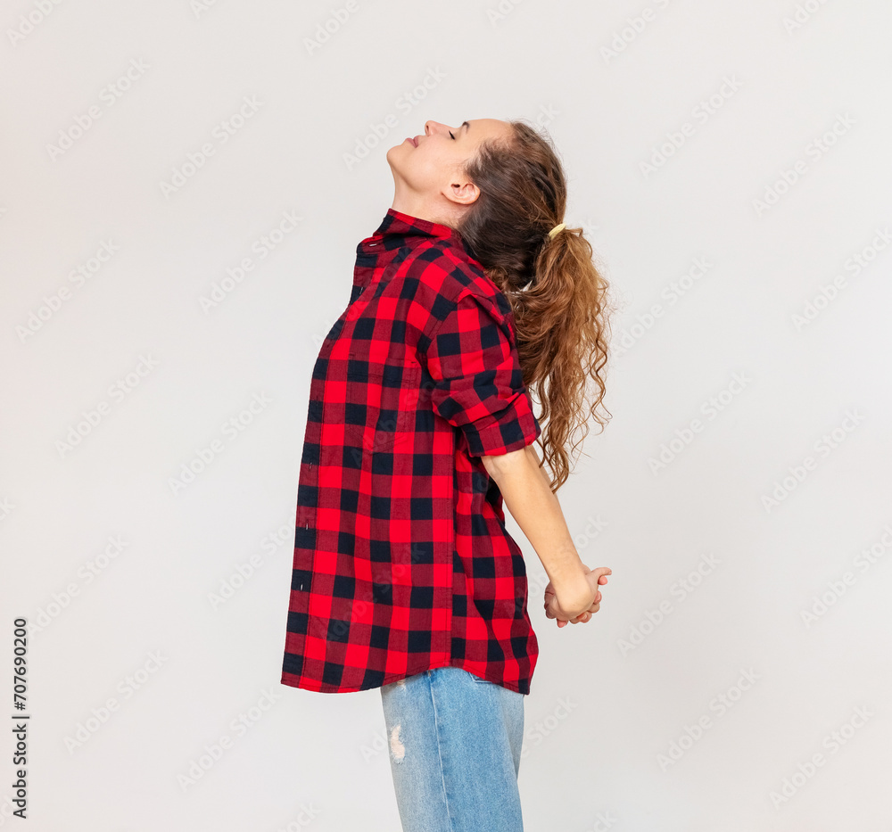 Brunette woman in red shirt stands in front of simple plain background and stretching her body. Brunette woman in red shirt stands in front of simple plain background and stretching her body.