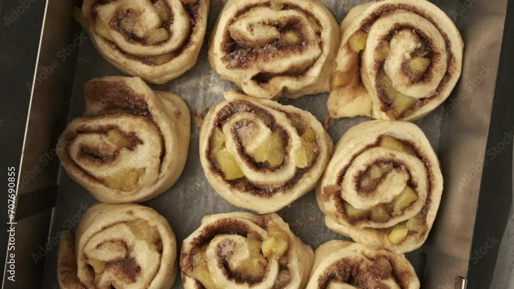 Fresh uncooked classic cinnamon buns on baking paper. Close up rotating shot of cinnabon rolls dough in a baking tray. The process of making traditional pastry Fresh uncooked classic cinnamon buns on baking paper. Close up rotating shot of cinnabon rolls dough in a baking tray. The process of making traditional pastry