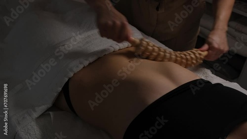 Woman having anti-cellulite massage session with madero therapy, professional therapist holding wooden roller in studio. photo