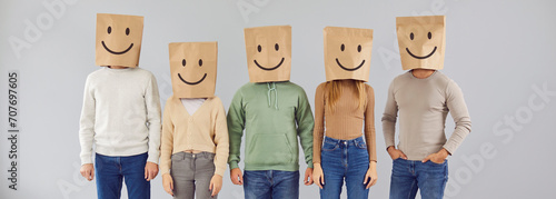 Portrait five casual male and female people with paper shopping package bags over heads with happy smiling emoticon mouth eyes facial expression drawn on them standing on gray color studio background photo