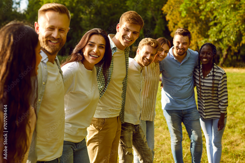Portrait of a group of happy people friends standing in a row in the summer park hugging and smiling. Young students looking cheerful at camera outdoors. Friendship and togetherness concept.