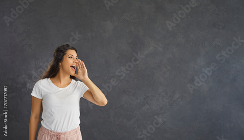 Woman standing on gray background loudly announces advertising, news or information about discounts. Caucasian casual young woman looking towards free space for text. Advertising concept. Banner.