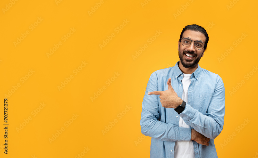 A charismatic man with a beard and glasses smiles and points sideways with his left hand A charismatic man with a beard and glasses smiles and points sideways with his left hand