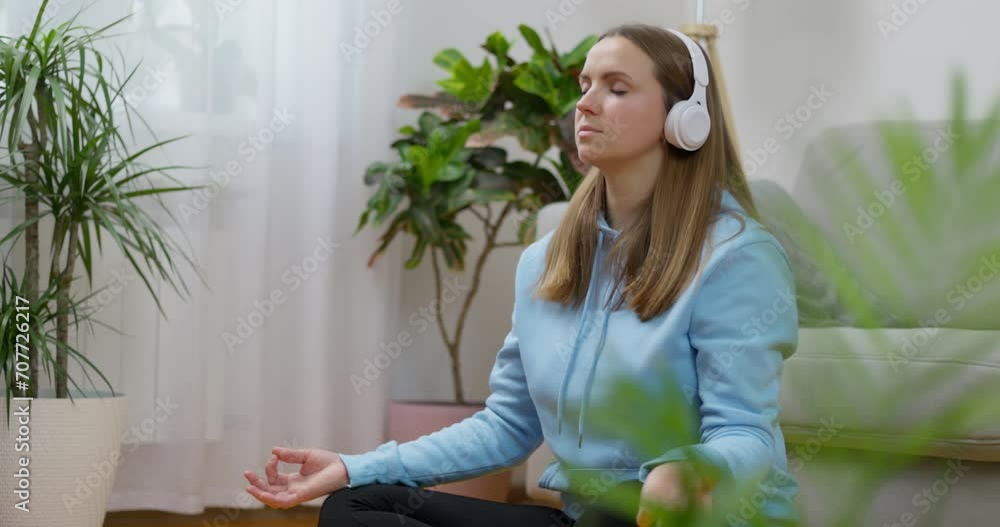 A happy young woman wearing headphones practicing yoga and meditation at home A happy young woman wearing headphones practicing yoga and meditation at home