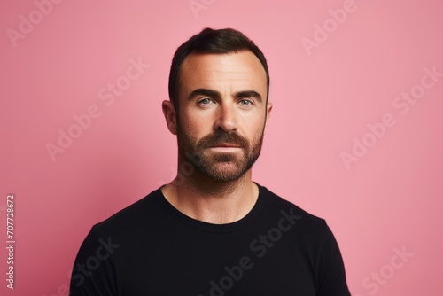 Portrait of handsome bearded man in black T-shirt, looking at camera, over pink background