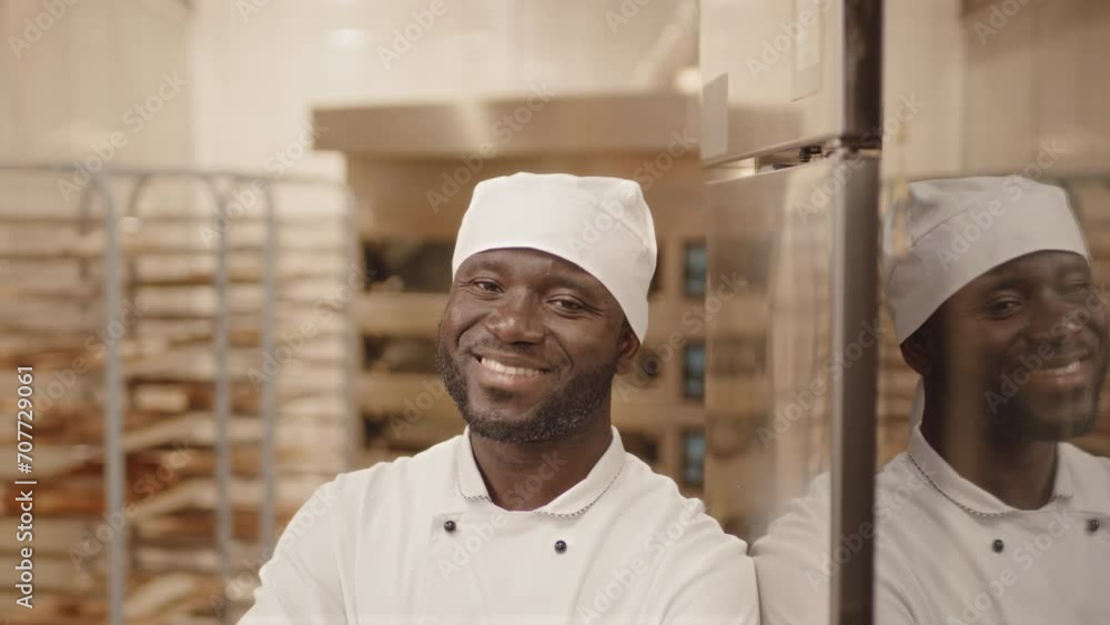 Waist up slowmo portrait of Black male chef baker posing with hands folded at camera while leaning on refrigerator in bakery kitchen Waist up slowmo portrait of Black male chef baker posing with hands folded at camera while leaning on refrigerator in bakery kitchen