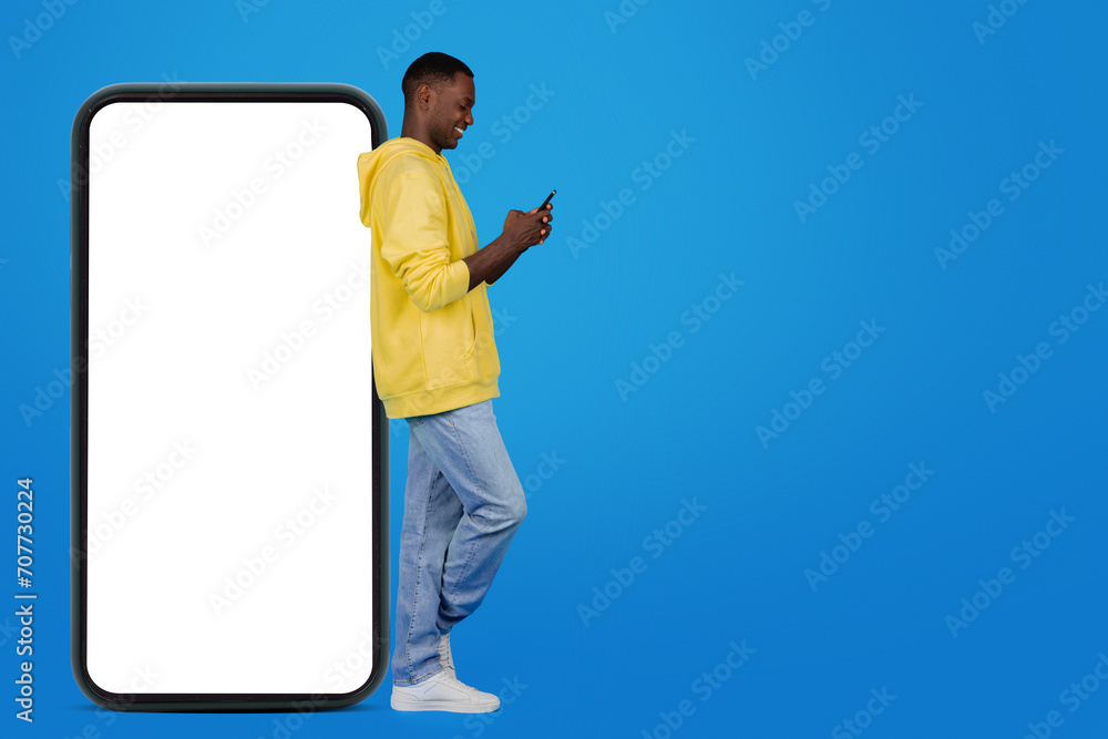 Φωτογραφία Content African American man in a yellow hoodie and light blue jeans uses his sm