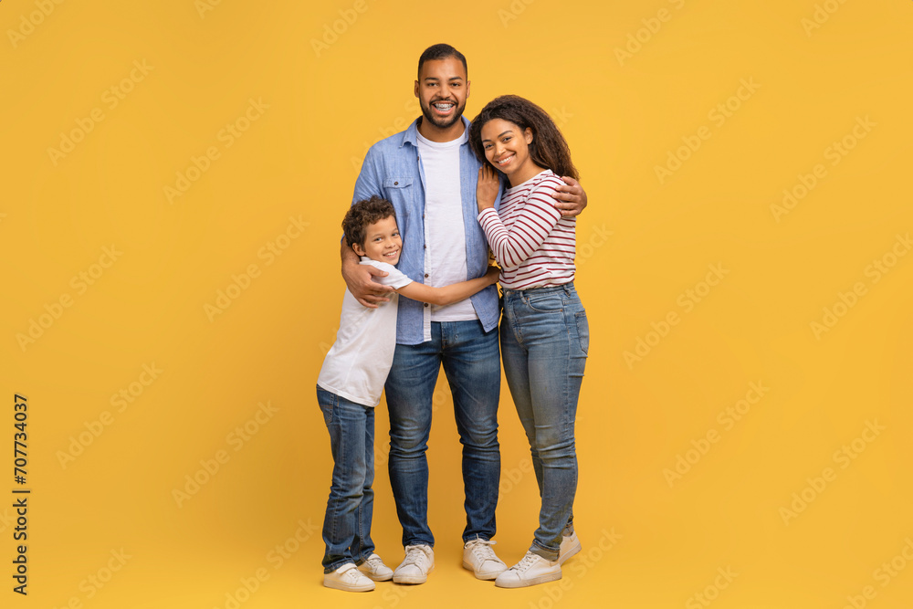 Family Portrait. Happy Black Parents And Preteen Son Embracing Over Yellow Background Family Portrait. Happy Black Parents And Preteen Son Embracing Over Yellow Background