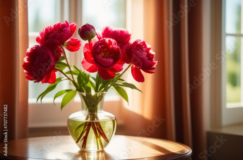 bouquet of flowers. red peonies in a transparent vase. bright modern interior, large window in the background. 