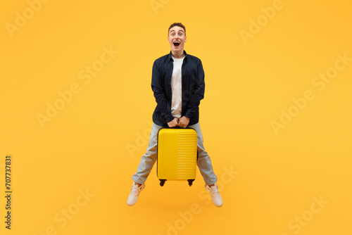 Excited guy tourist jumping in the air with suitcase