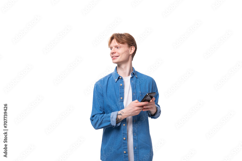 portrait of a smiling caucasian red-haired guy in a denim blue shirt with a smartphone in his hand portrait of a smiling caucasian red-haired guy in a denim blue shirt with a smartphone in his hand