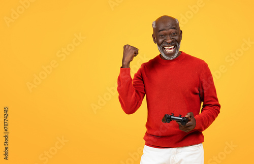 Joyful senior Black man with a game controller in hand, celebrating a win with a cheerful fist pump