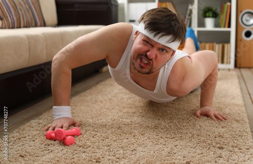 A young handsome man with excess weight makes the first fitness training at home on the carpet is wrung out and he ery heavily loaded does not stimulate to lose weight. photo