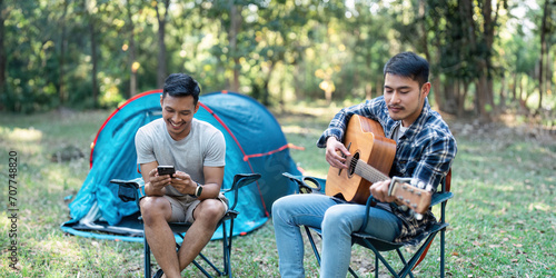 LGBTQIA Gay couple camping together in woods for holidays and relax on guitar together