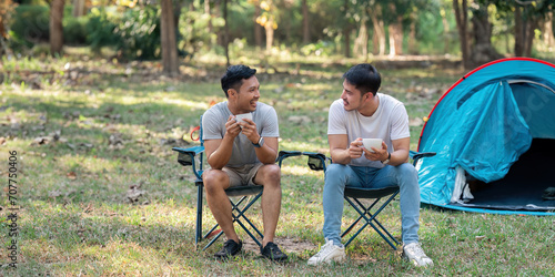 Gay LGBTQIA couple sitting on picnic chair drinking tea and coffee while camping on vacation holiday