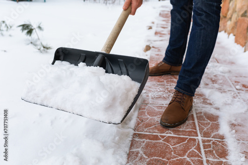 A man removes snow with a shovel from the path near the house