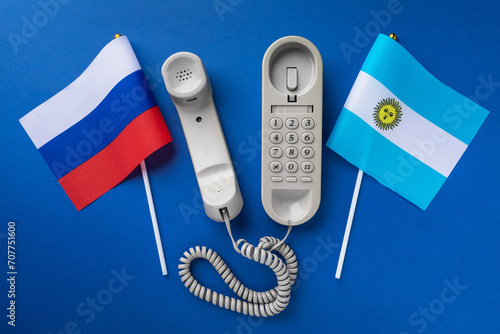 Old telephone and two flags on a blue background, concept on the theme of telephone conversations between Argentina and Russia