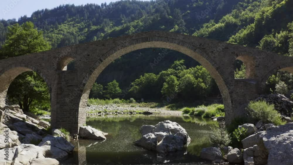Approaching drone shot passing through the main arch of the Devil's Bridge over the Arda River located in the town of Ardino near the Rhodope Mountains in Bulgaria. Approaching drone shot passing through the main arch of the Devil's Bridge over the Arda River located in the town of Ardino near the Rhodope Mountains in Bulgaria.
