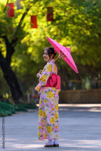 A young woman wearing a Japanese traditional kimono or yukata holding an umbrella is happy and cheerful in the park.