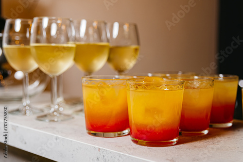 Tequila Sunrise and White Wine Selection. An array of Tequila Sunrise cocktails with gradient orange hues and white wine in stemmed glasses, ready for a party.