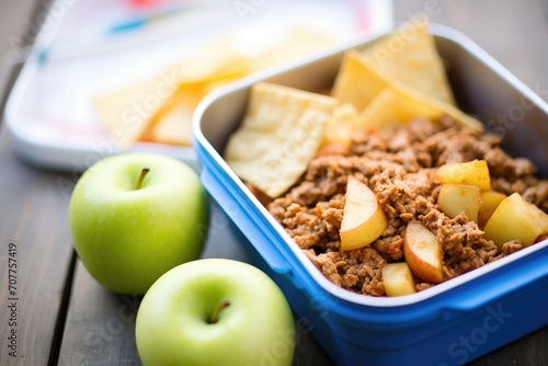 sloppy joe in a lunchbox, alongside apple and chips photo